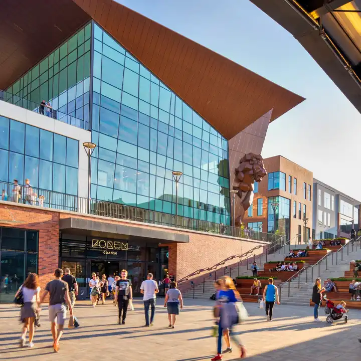 Besökare promenerar utanför den moderna gallerian Forum Shopping i Gdansk med dess stora glasfasader och karaktäristiska arkitektur.