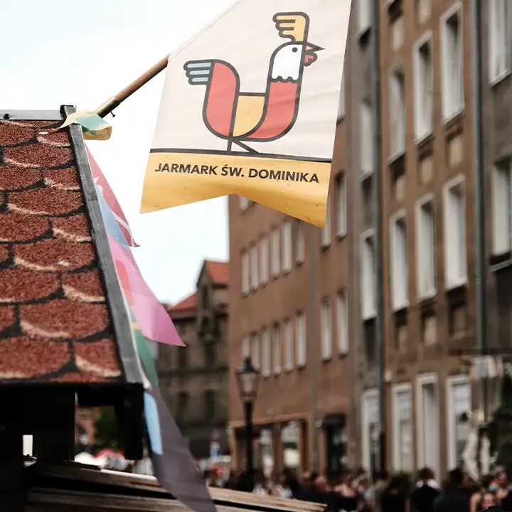 En flagga med en tupp-symbol och texten Jarmark św. Dominika vajar ovanför ett marknadsstånd under den kända St Dominics marknad i Gdańsk.