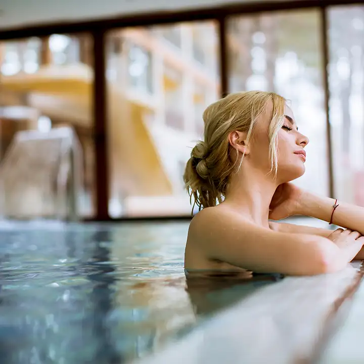 En kvinna som kopplar av i en lyxig inomhuspool på ett spa i Gdansk eller Sopot, med utsikt genom stora fönsterpartier.
